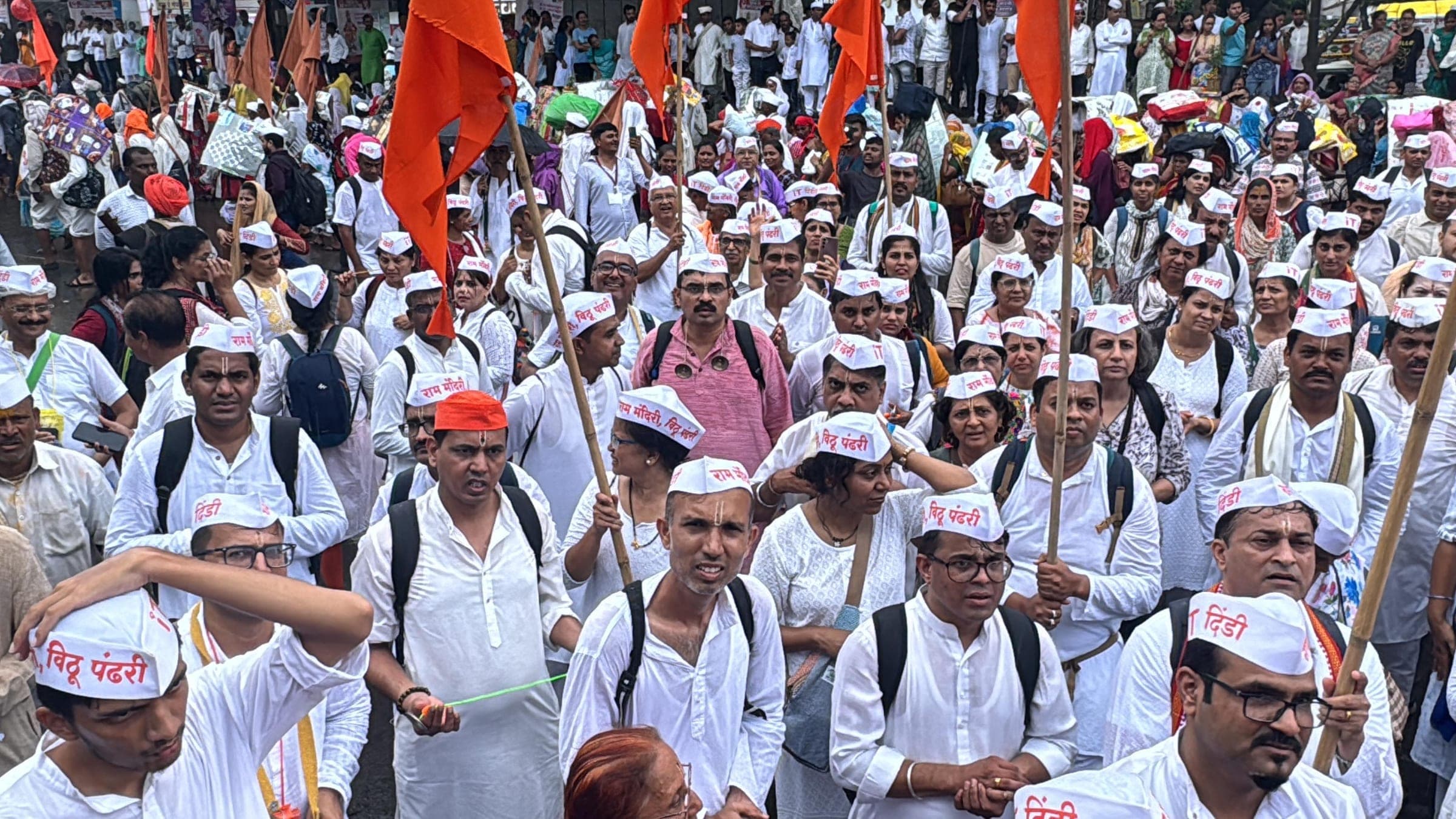 Warkari dindi walkers in white kurtas and Gandhi caps with saffron flags raised, on the Pune to Saswad stretch of the annual Wari