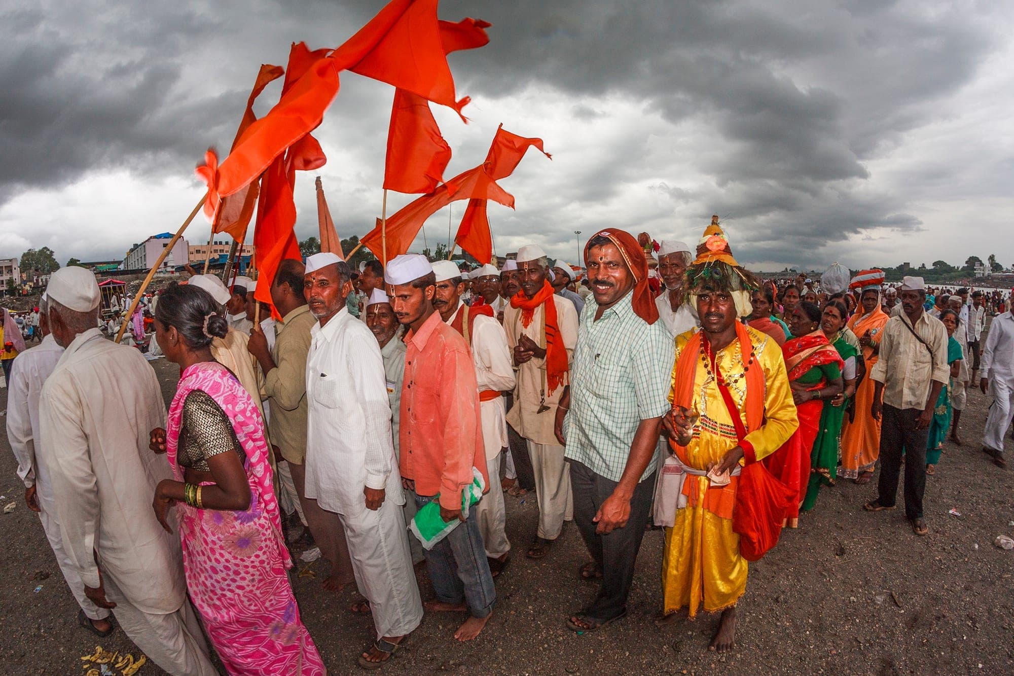 A small dindi of Varkari pilgrims on the yatra to Pandharpur, saffron flags raised, under a monsoon sky